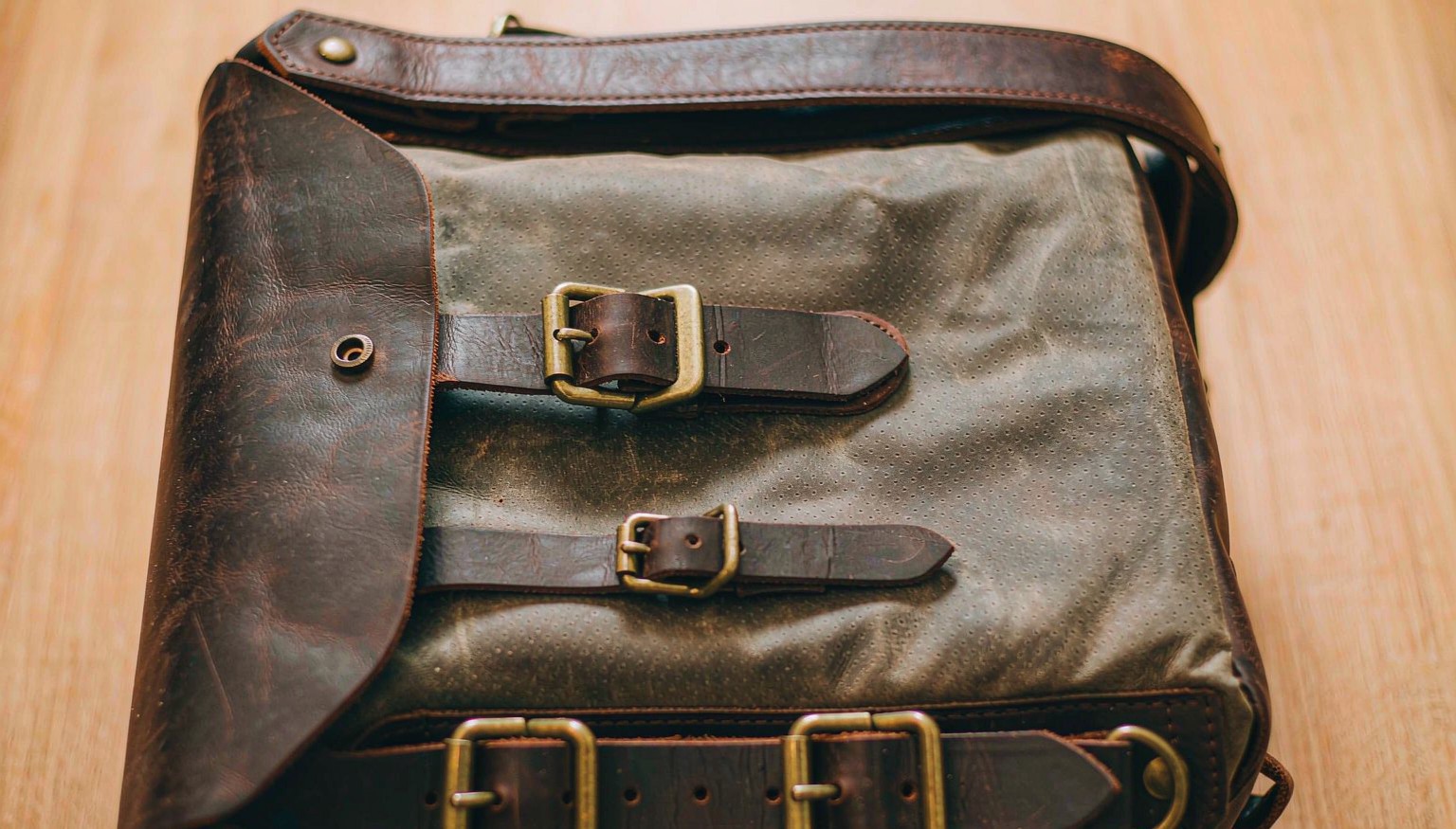 Close-up of a waxed canvas motorcycle tank bag with brass buckles and leather trim